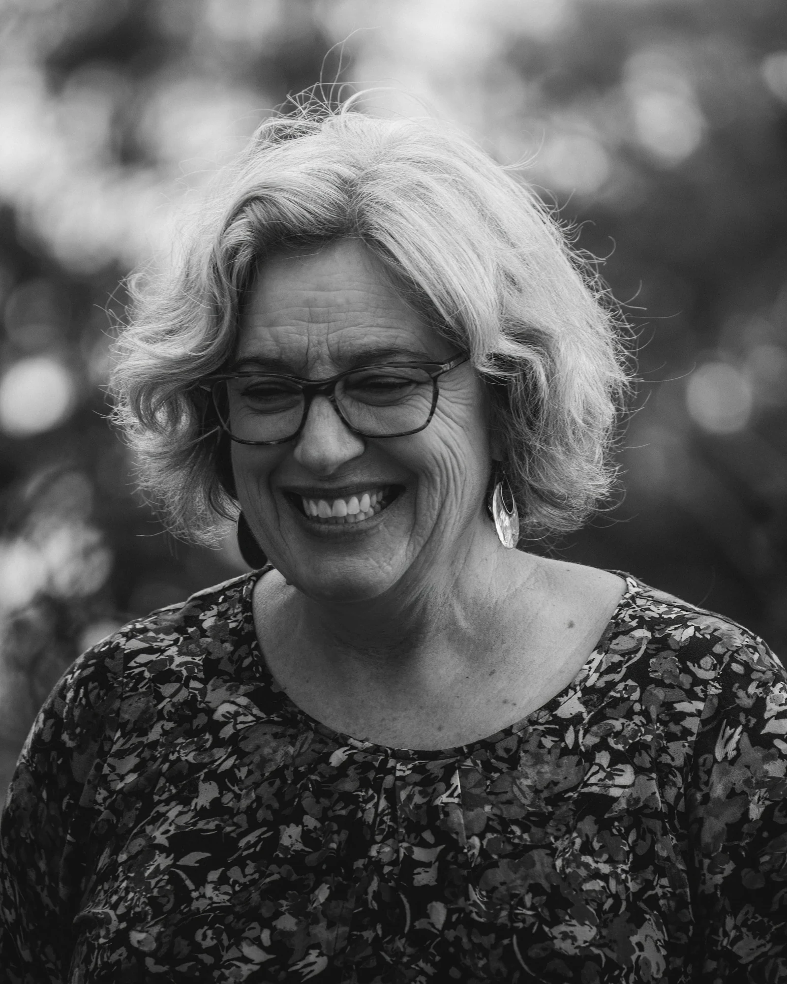A black and white portrait of a smiling person with glasses