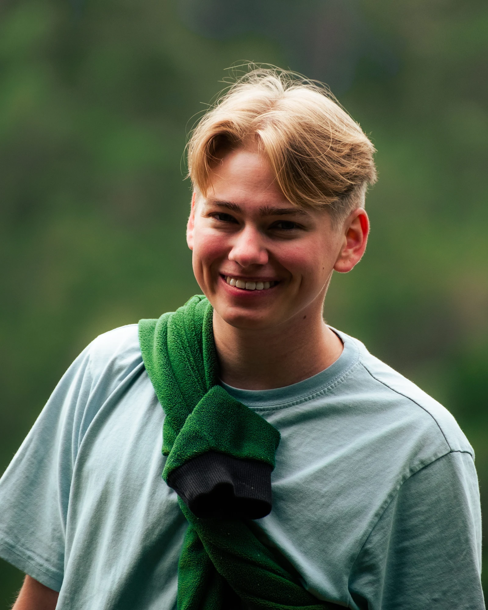 A smiling person in a green shirt with soft green foliage behind them