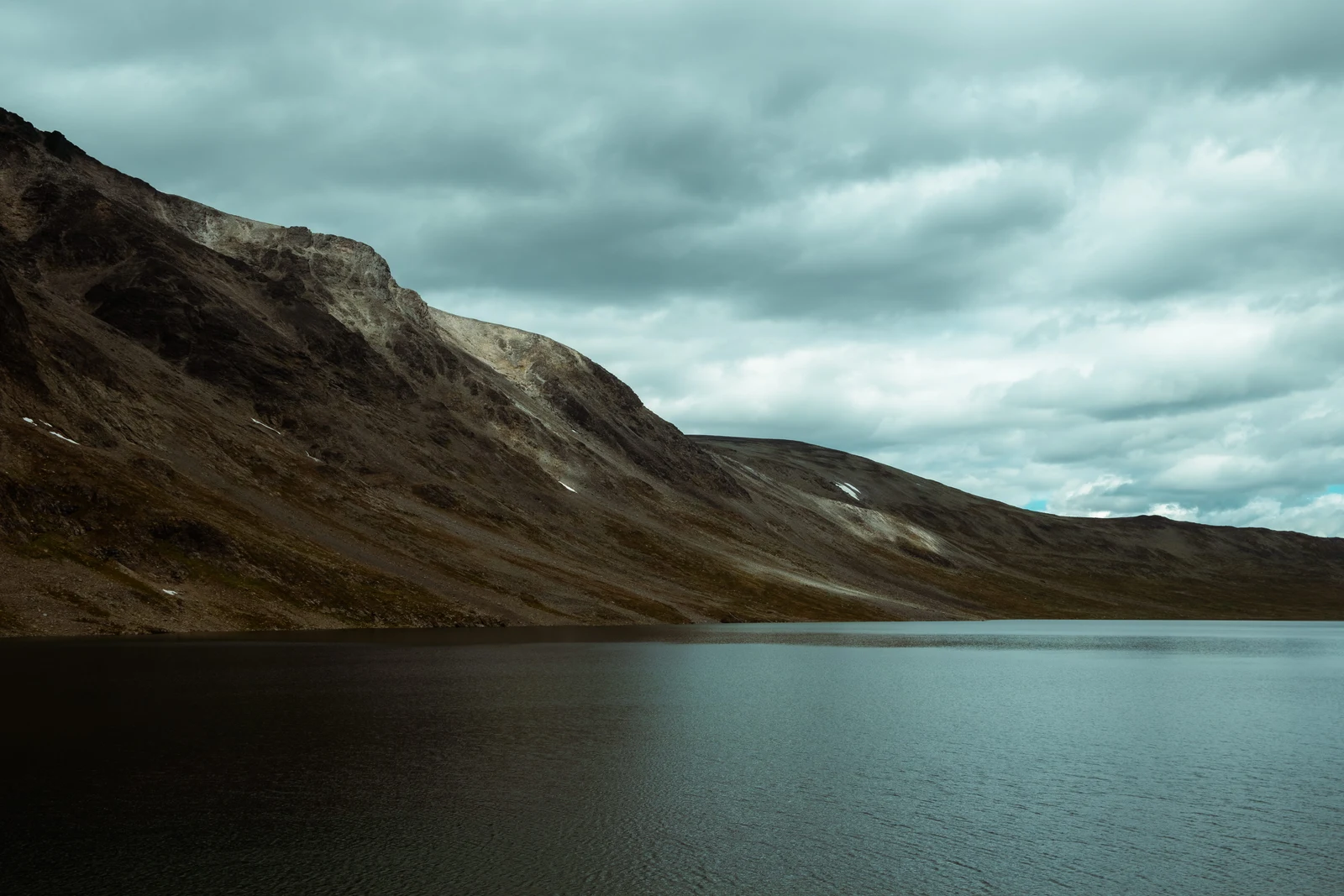 A steep mountain rising above a still lake beneath dramatic clouds