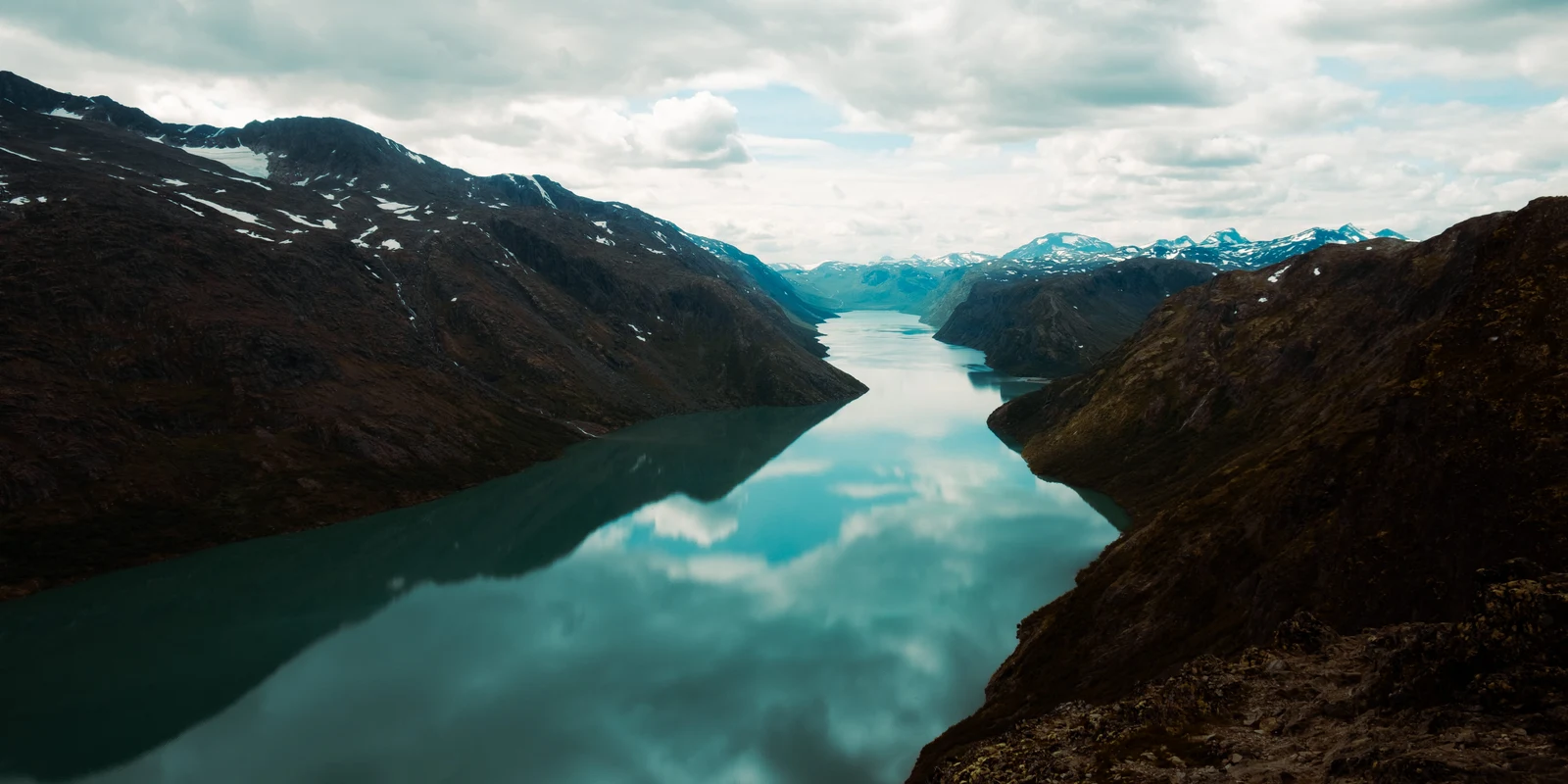 A long turquoise lake reflecting clouds between mountain slopes