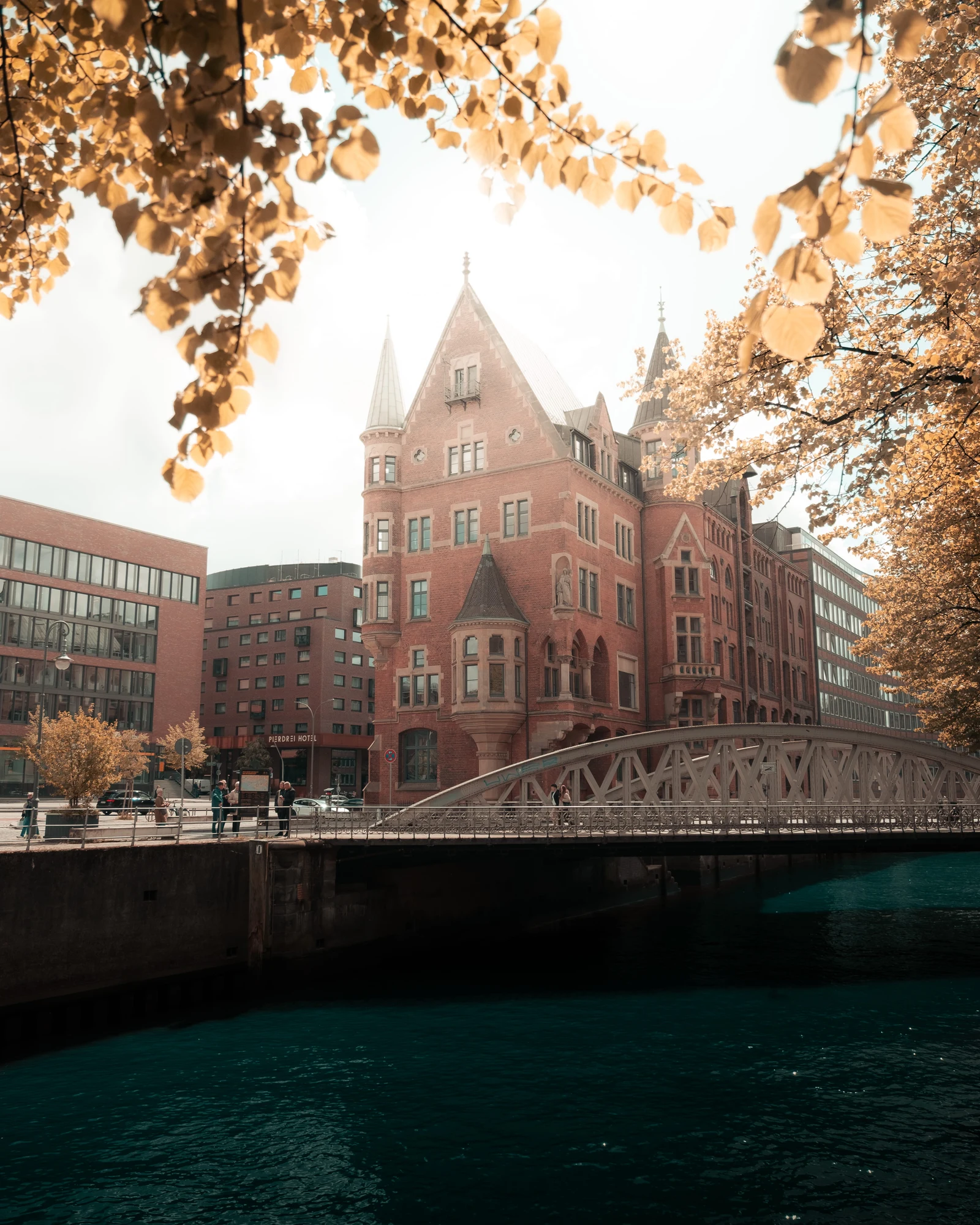 A red brick waterside building and bridge framed by golden leaves