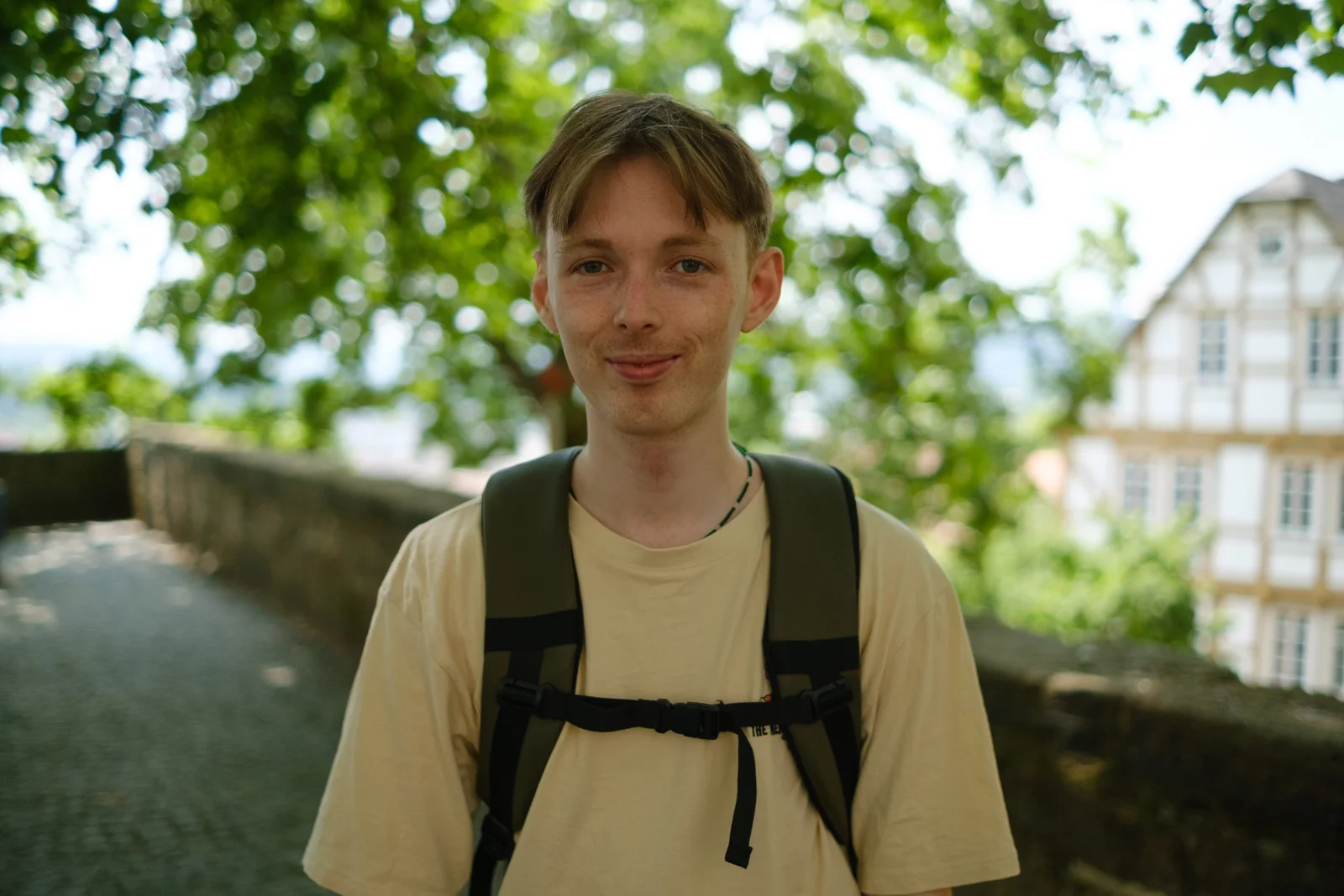 areal alien wearing a pale T-shirt and backpack beneath leafy trees