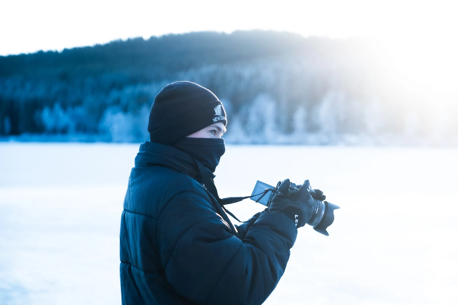 A person in dark winter clothing standing beside a snowy lake