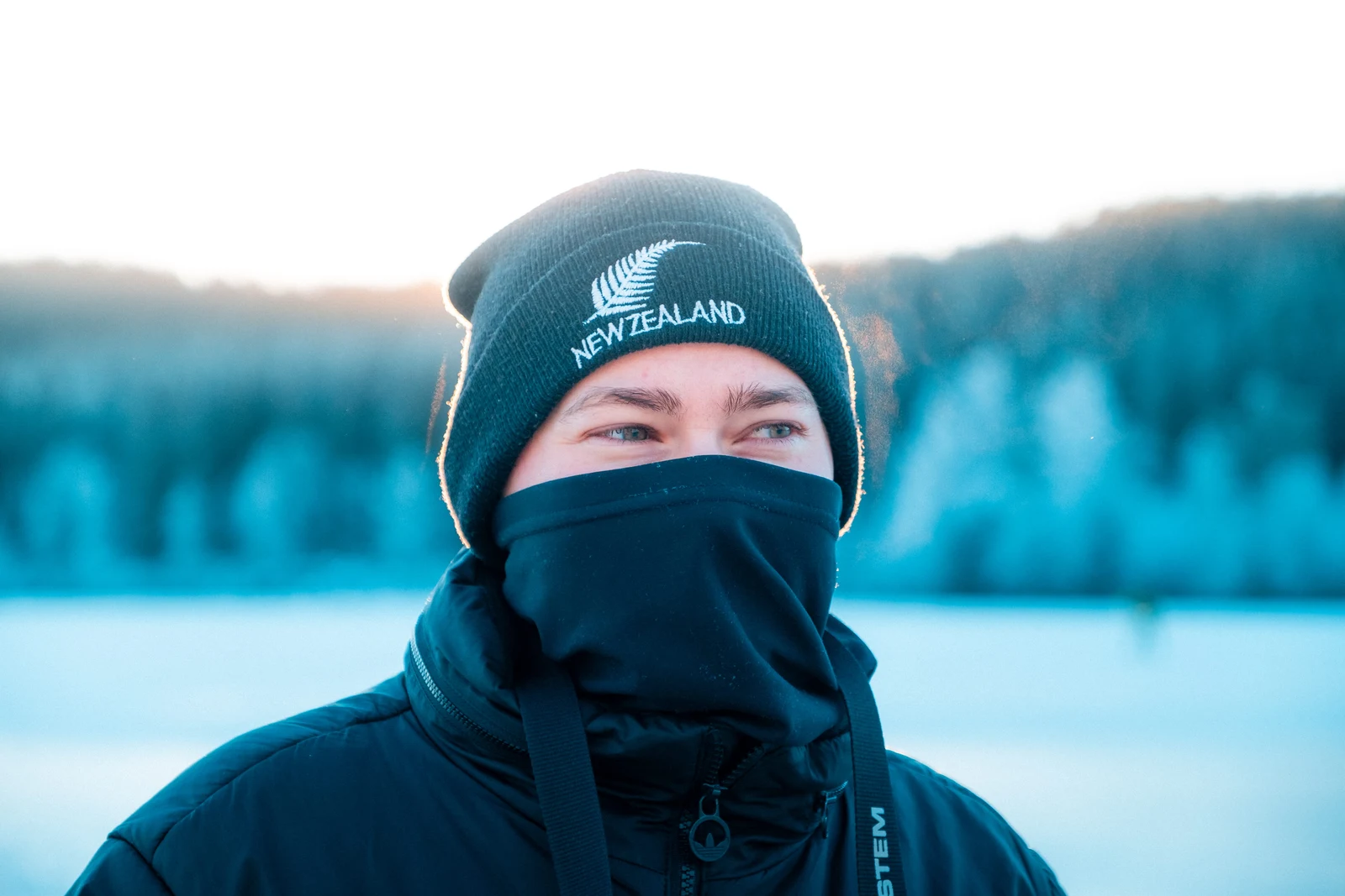 A person wearing a winter hat and face covering beside a snowy landscape