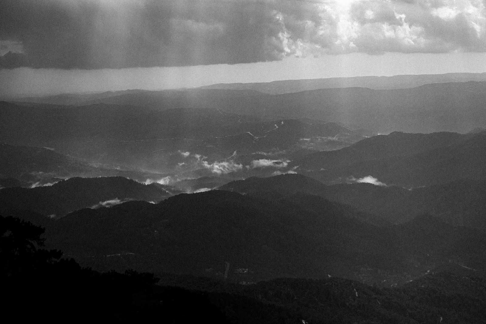 A black and white view of layered hills beneath shafts of light
