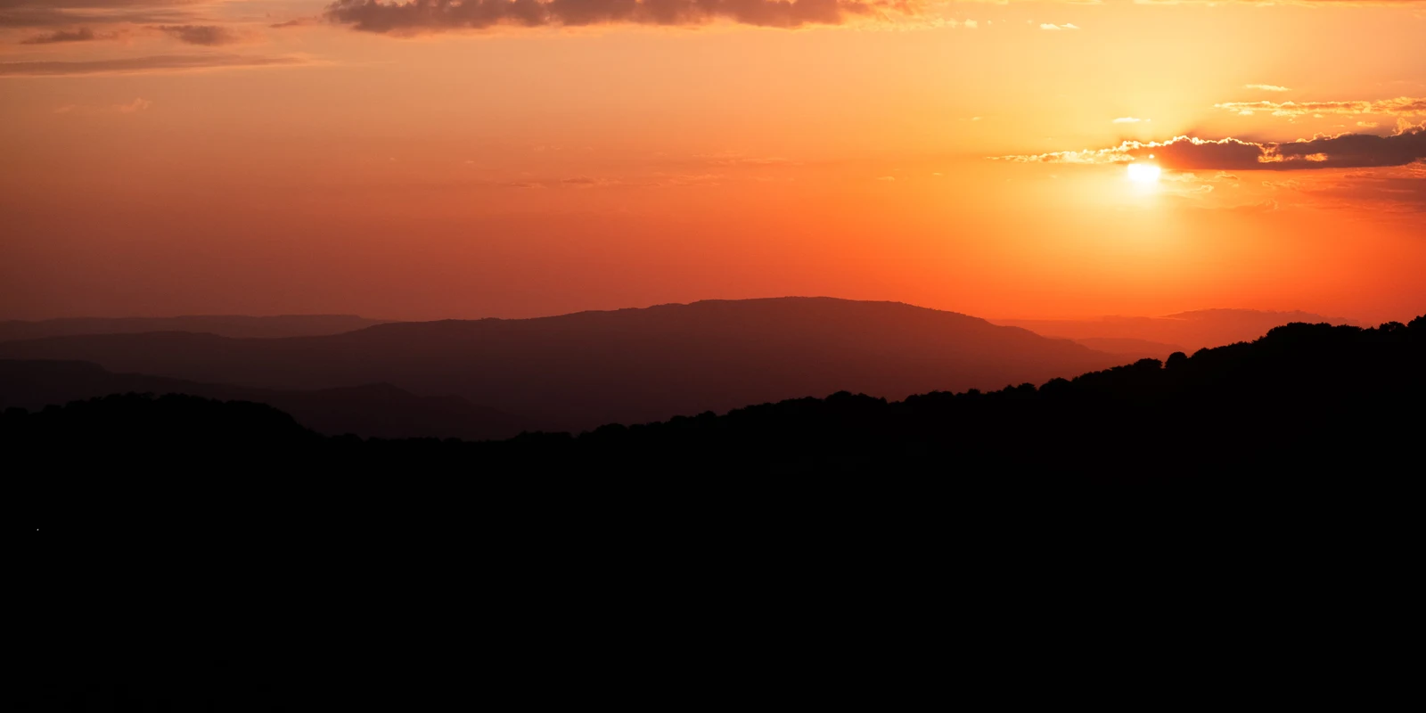 An orange sunset above the silhouettes of distant hills