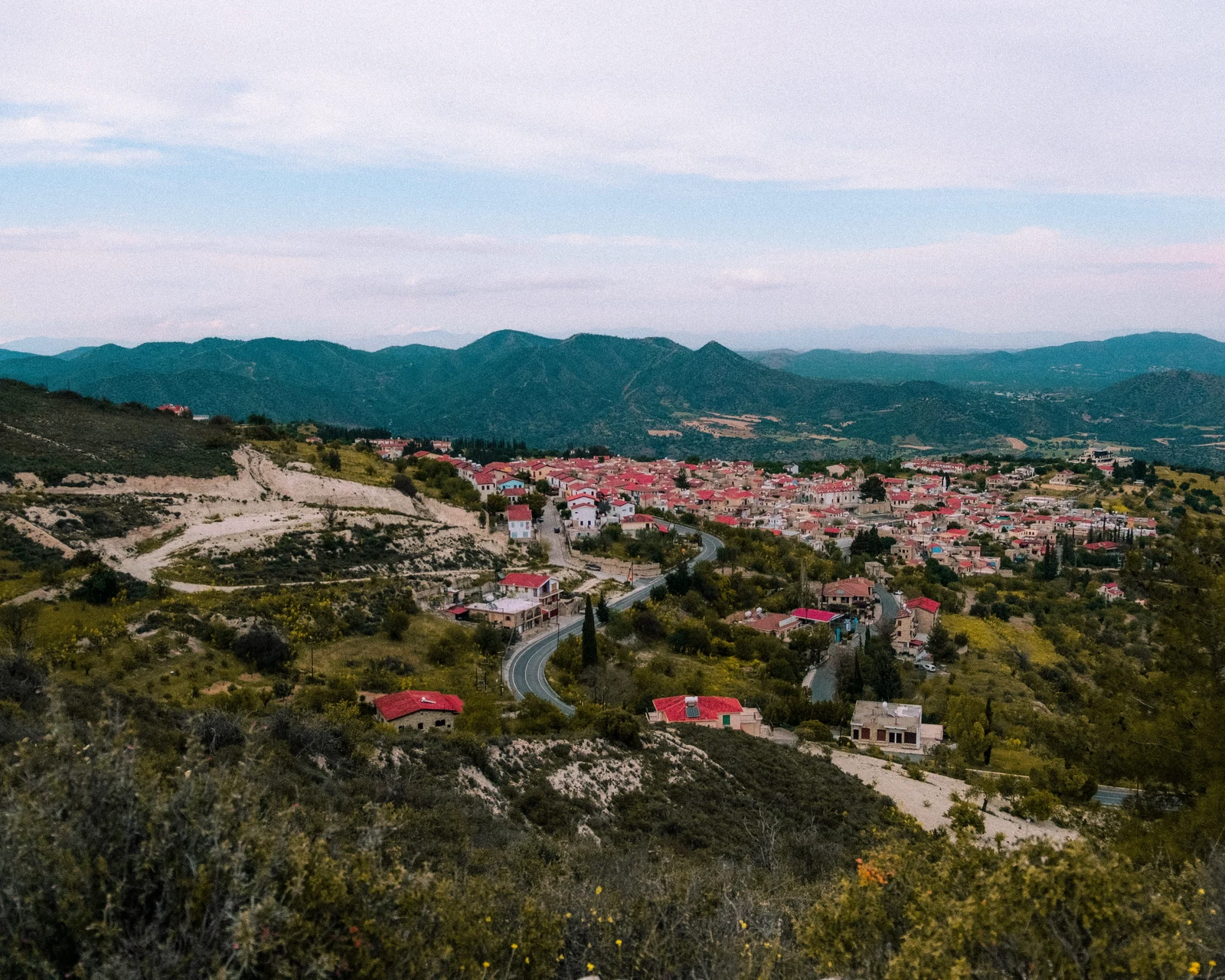 A hillside town with pale buildings and red roofs beneath distant mountains