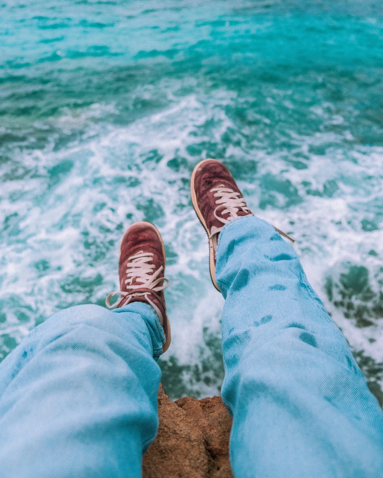 Sneakers and pale trousers above bright turquoise waves