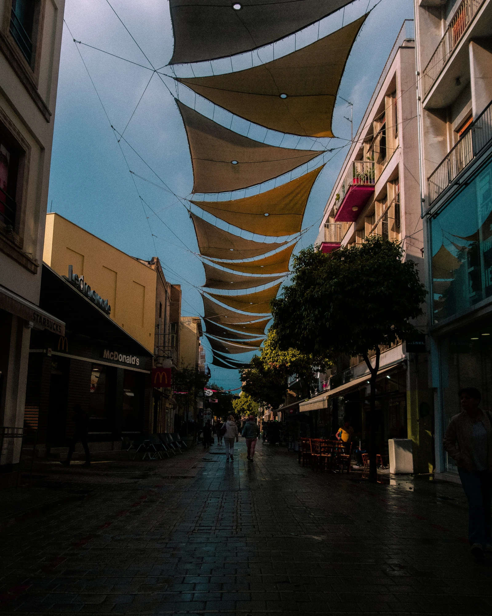 A pedestrian street shaded by fabric sails stretched between buildings