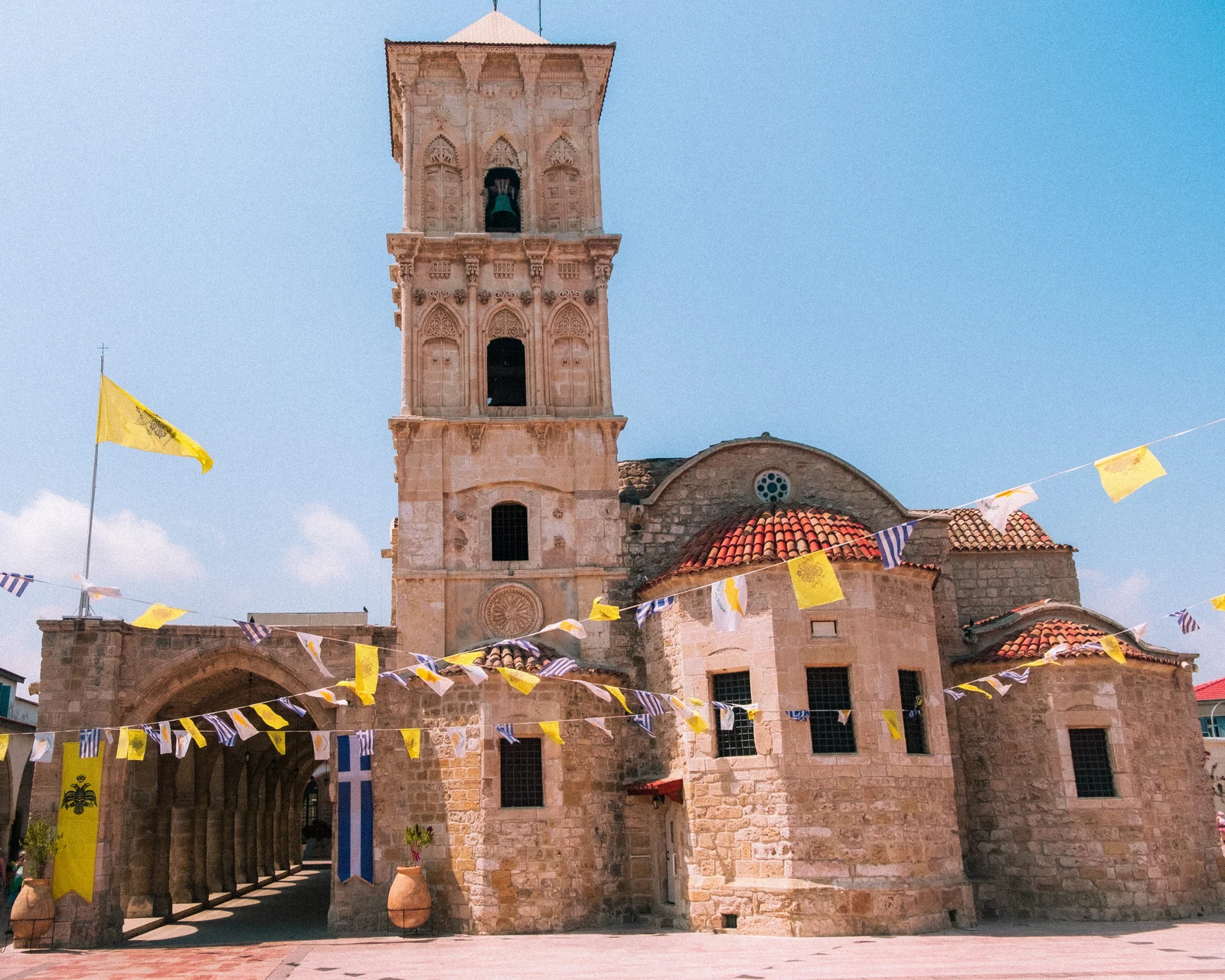 A stone church and bell tower decorated with yellow flags beneath blue sky