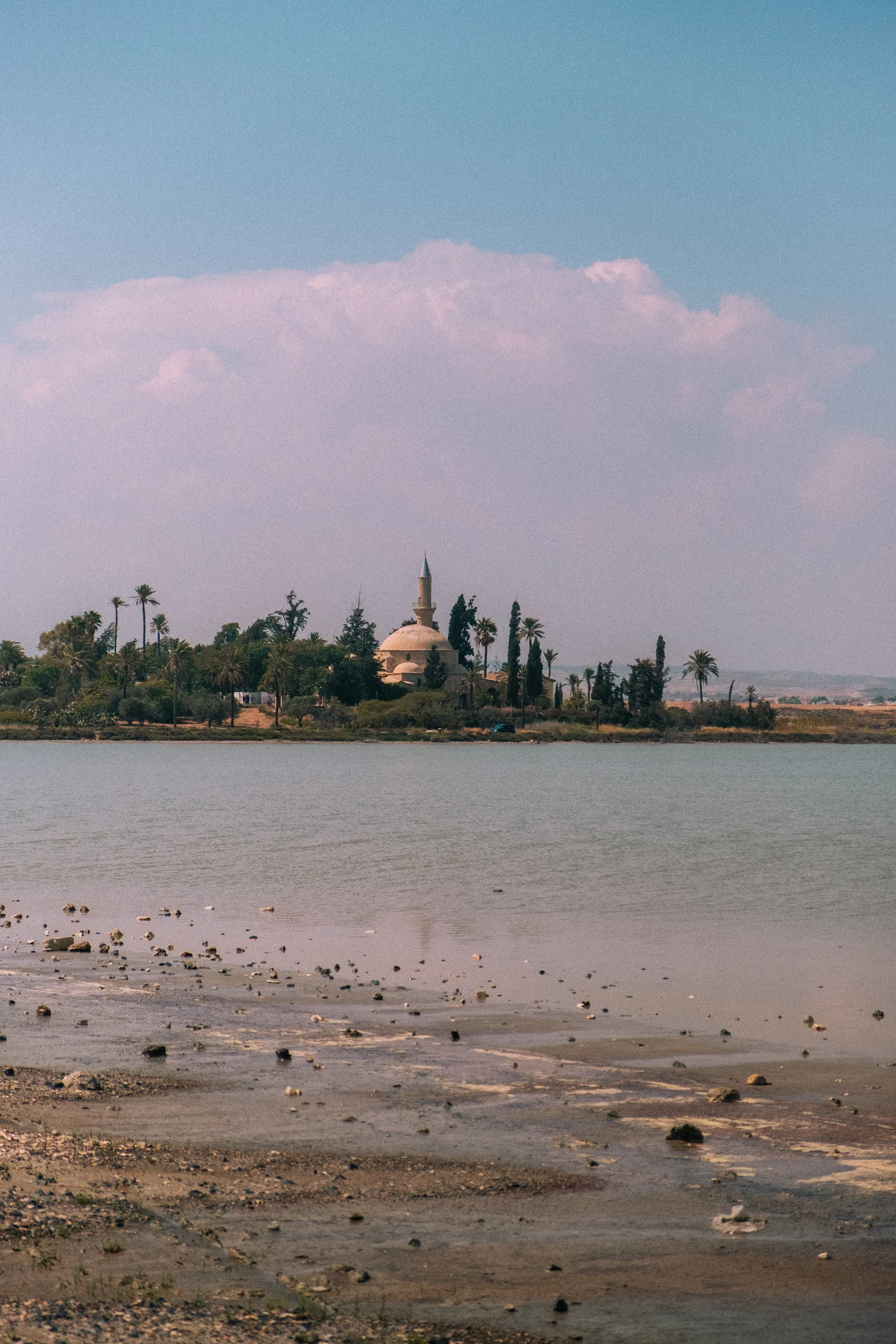 A distant waterfront building beyond tidal sand beneath pink clouds