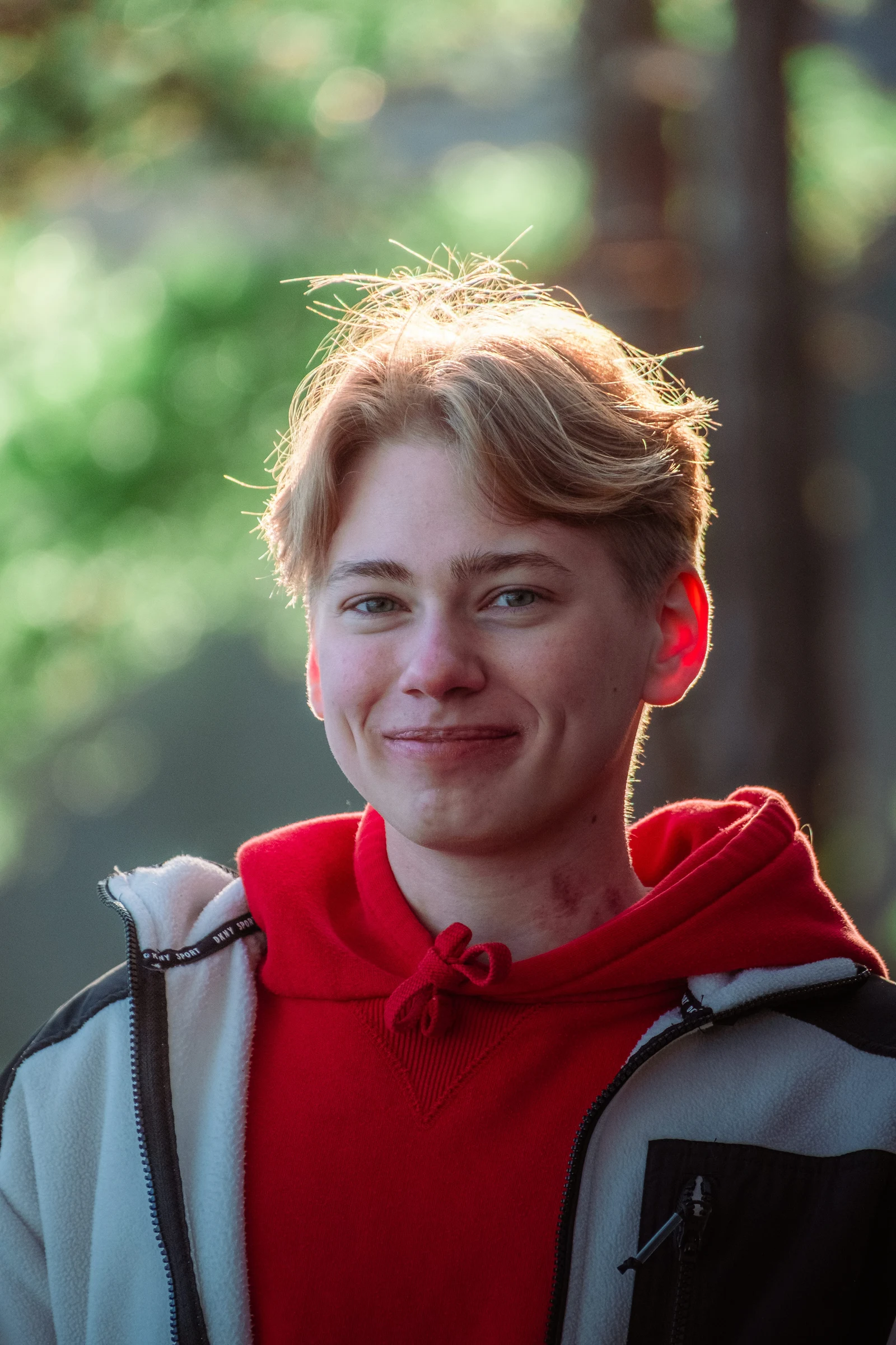 A person in a red hoodie looking to the side in a sunlit woodland