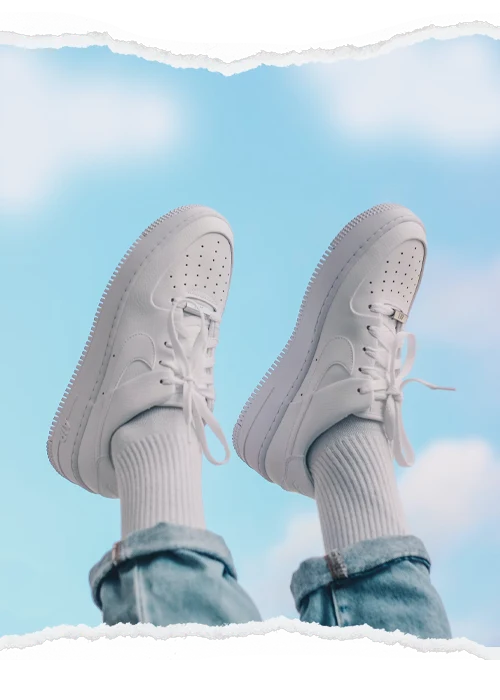 White sneakers against a blue sky, framed by a torn-paper photographic border