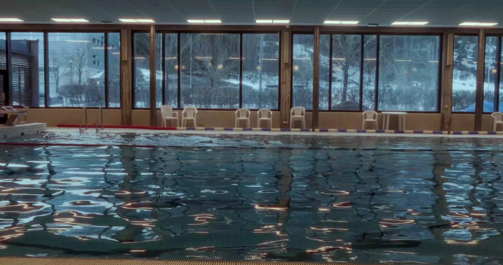 An indoor swimming pool with winter trees beyond the windows